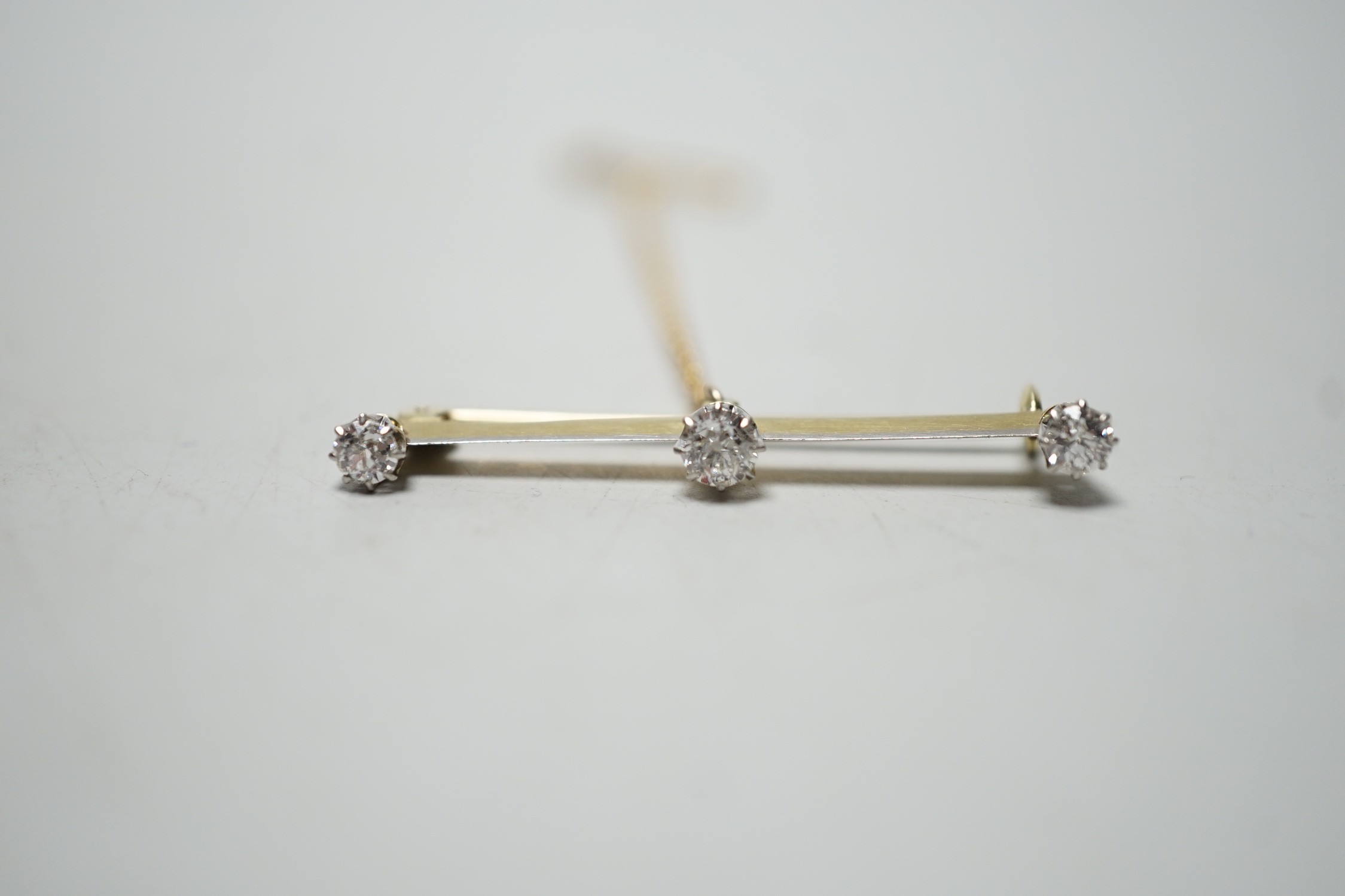 A yellow metal and three stone diamond set bar brooch, 36mm, gross weight 2.8 grams.